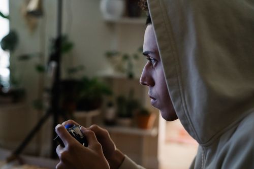 Free Side view of crop focused ethnic male gamer with console controller playing video game while looking forward in house Stock Photo