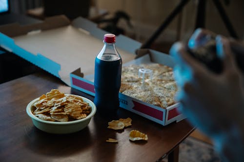 Crop person at table with potato chips and cola