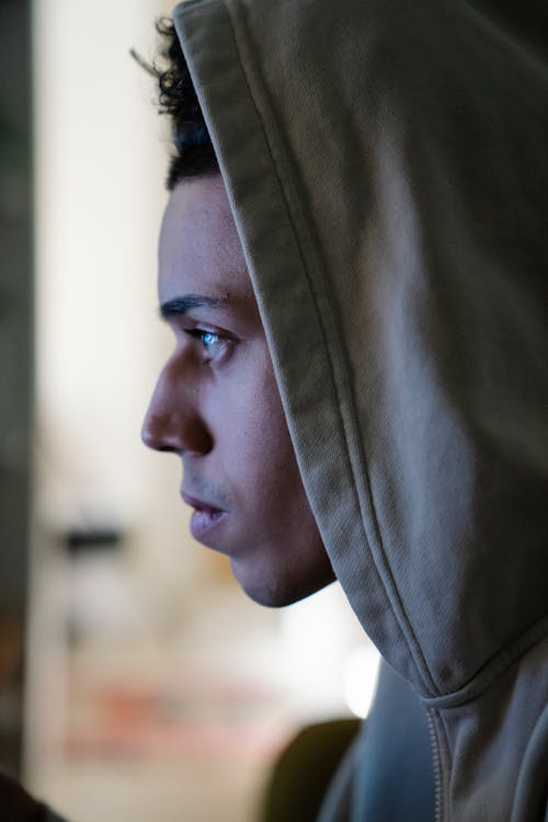 Side view of focused young ethnic male in hoodie looking forward in house on blurred background