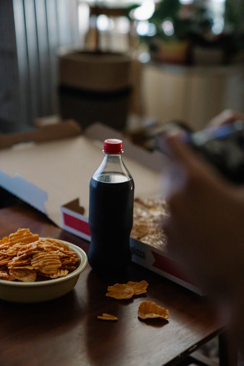 Free Crop person at table with carbonated drink and potato chips Stock Photo