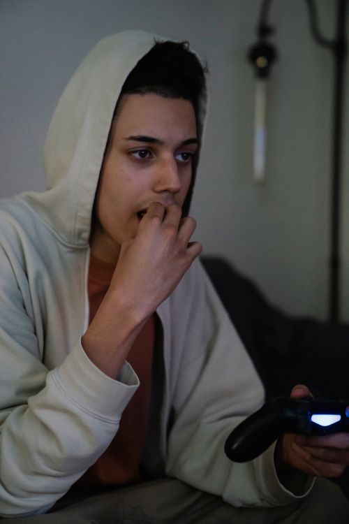 Free Young attentive ethnic male gamer in hoodie with joystick looking forward while playing video game in house Stock Photo