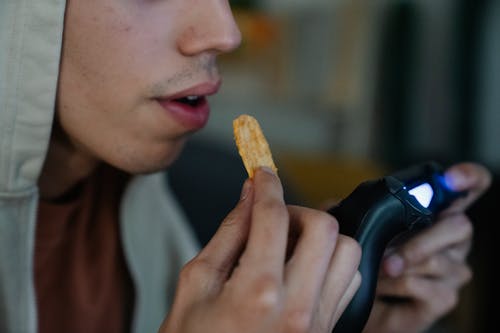 Crop gamer with potato chip and gamepad at home