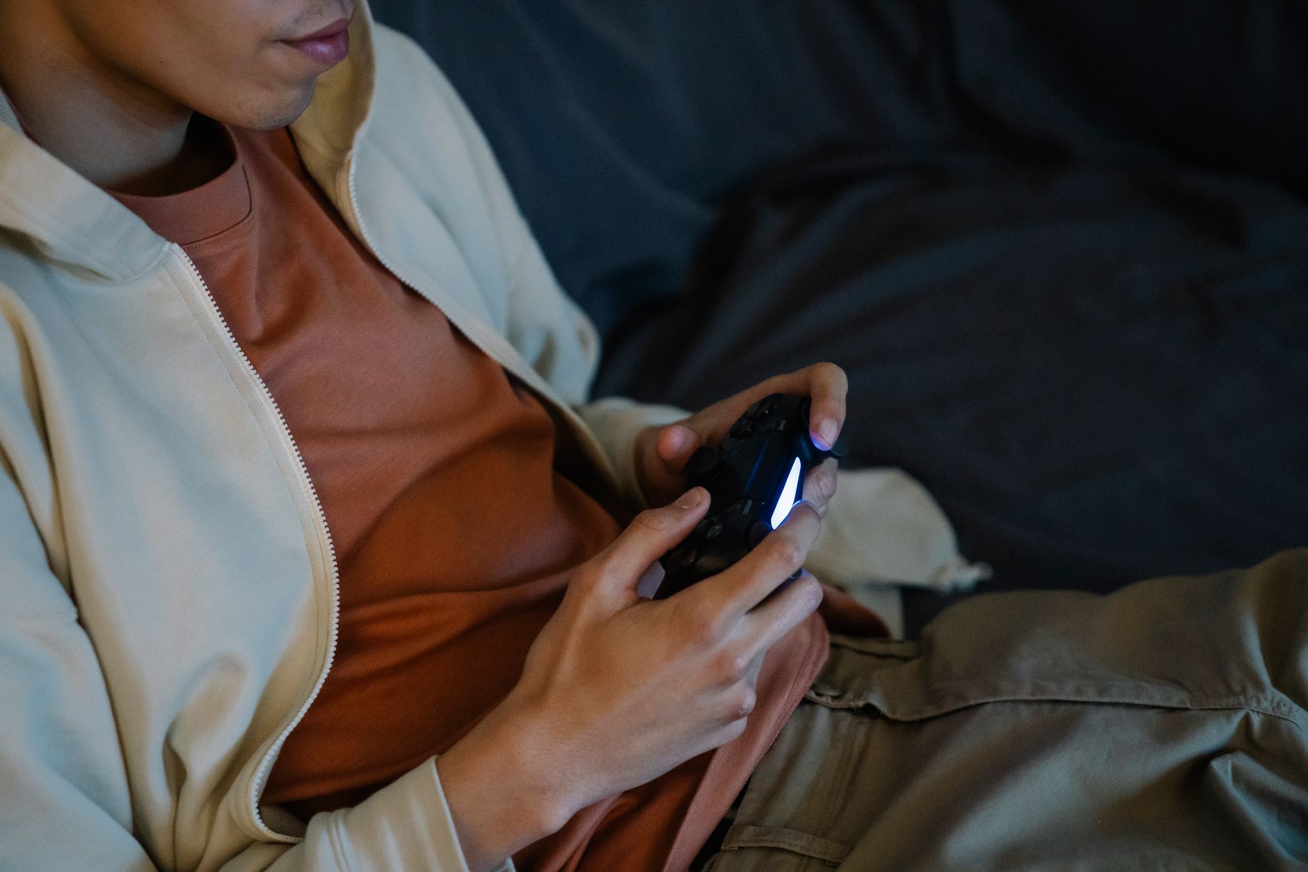 Crop anonymous man with console controller playing video game while sitting on couch in house