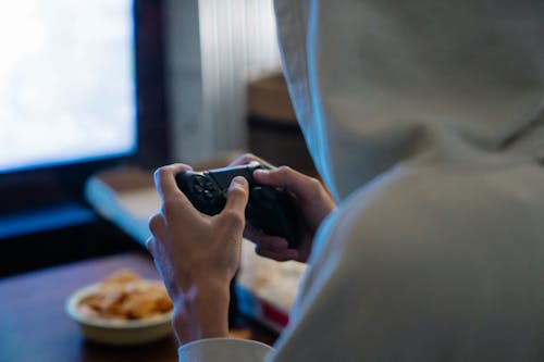 Crop gamer with console controller playing video game in room