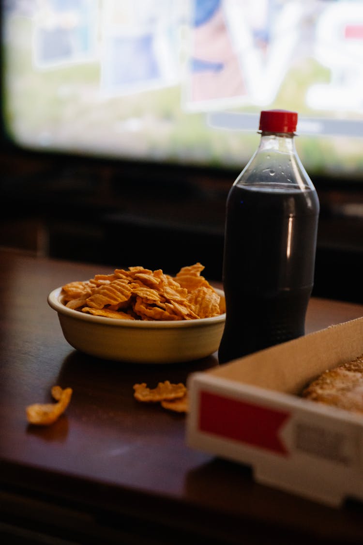 Bottle Of Soft Drink Near Potato Chips Against Monitor