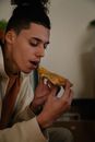 Cool young ethnic male with modern haircut enjoying yummy pie piece in house room