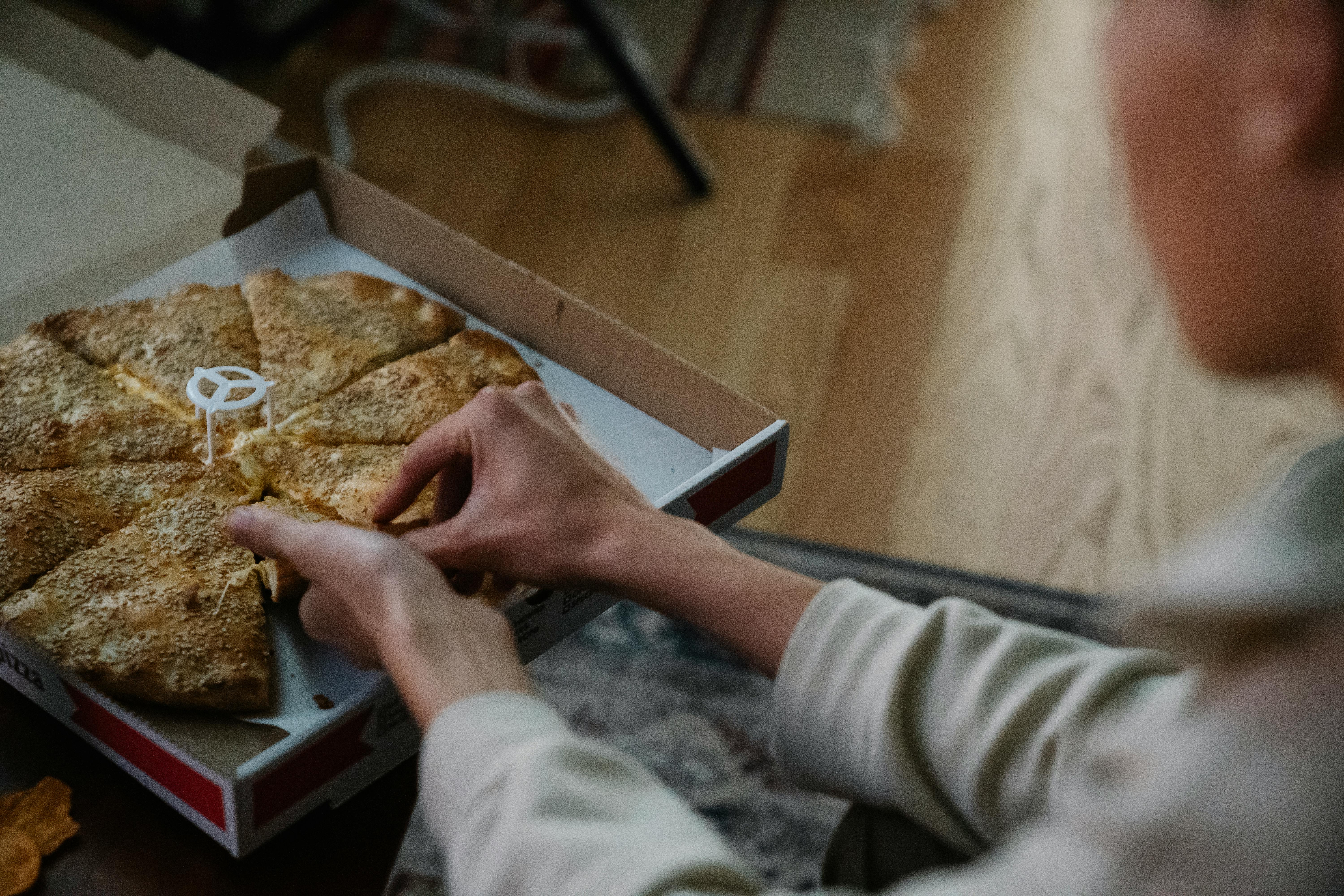 unrecognizable person taking slice of pizza from box