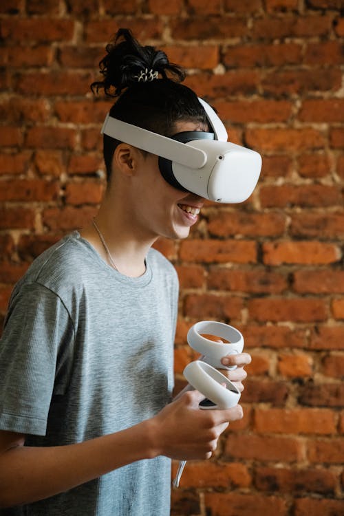 Free Side view of male teen in modern glasses smiling while experiencing virtual reality and playing videogame Stock Photo
