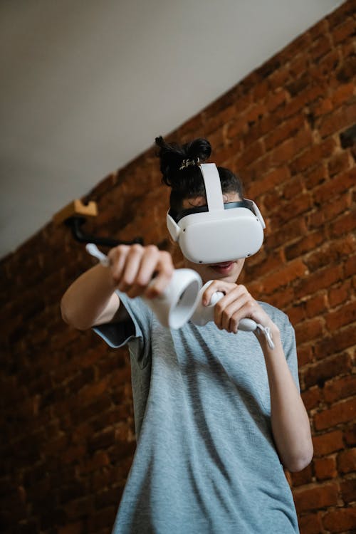 Free Anonymous male teen in VR googles playing game with controllers in hands towards camera Stock Photo