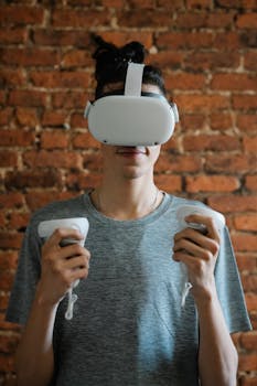 Young male standing near brick wall and smiling while playing video game and using VR headset and controllers