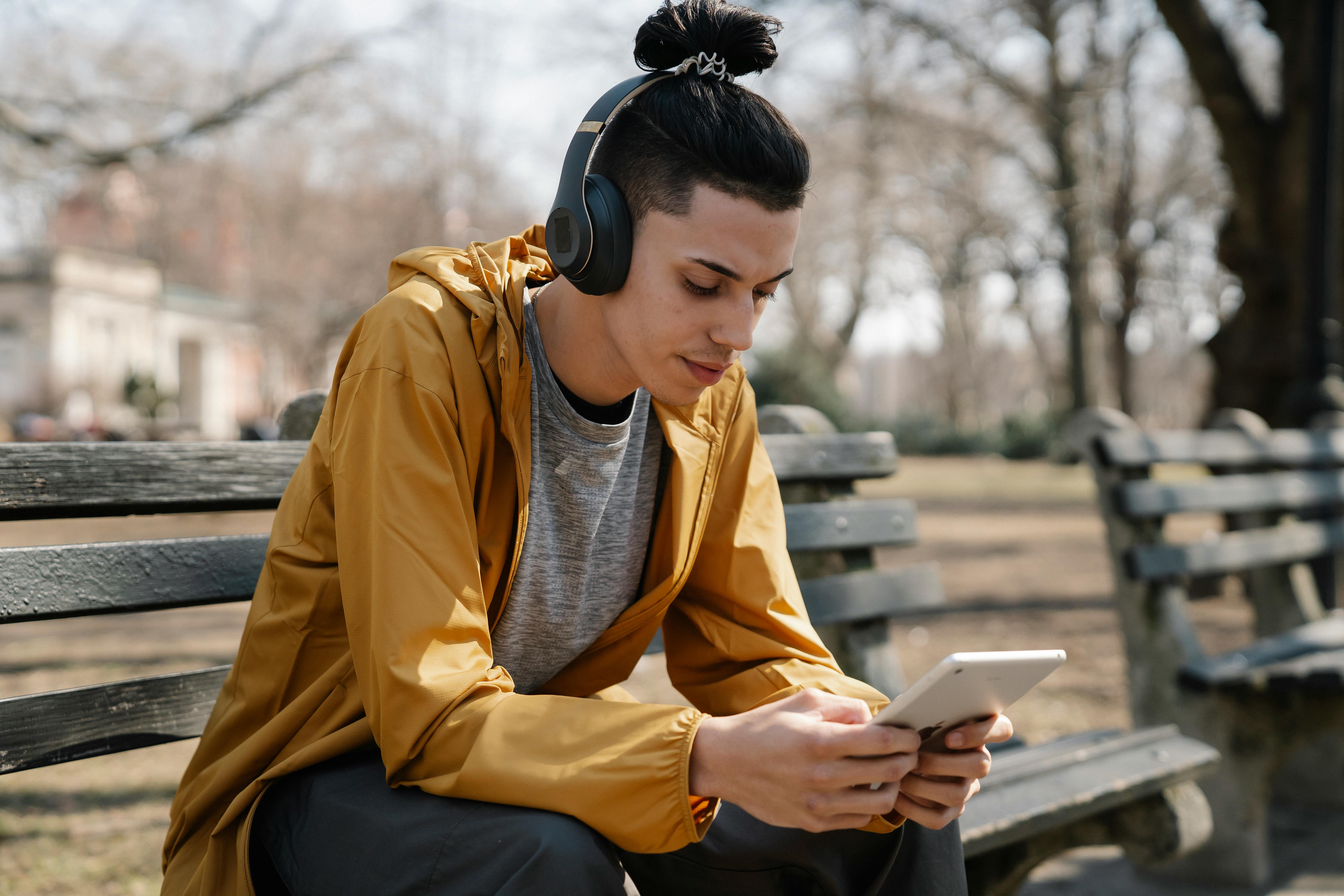 Young ethnic woman in TWS earphones using smartphone on bench in