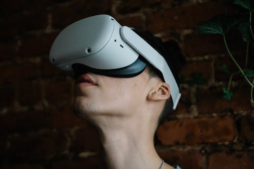 Young male wearing modern goggles of virtual reality and immersing in cyberspace while being in room with brick walls