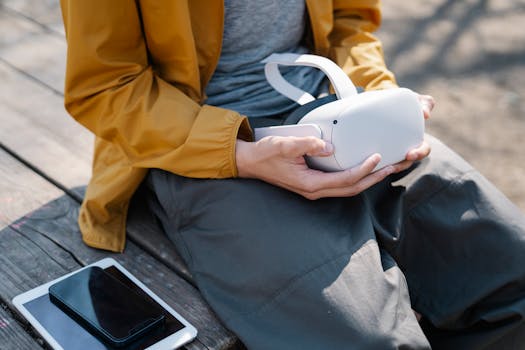 Person sitting on a park bench holding a VR headset with a tablet and smartphone nearby.
