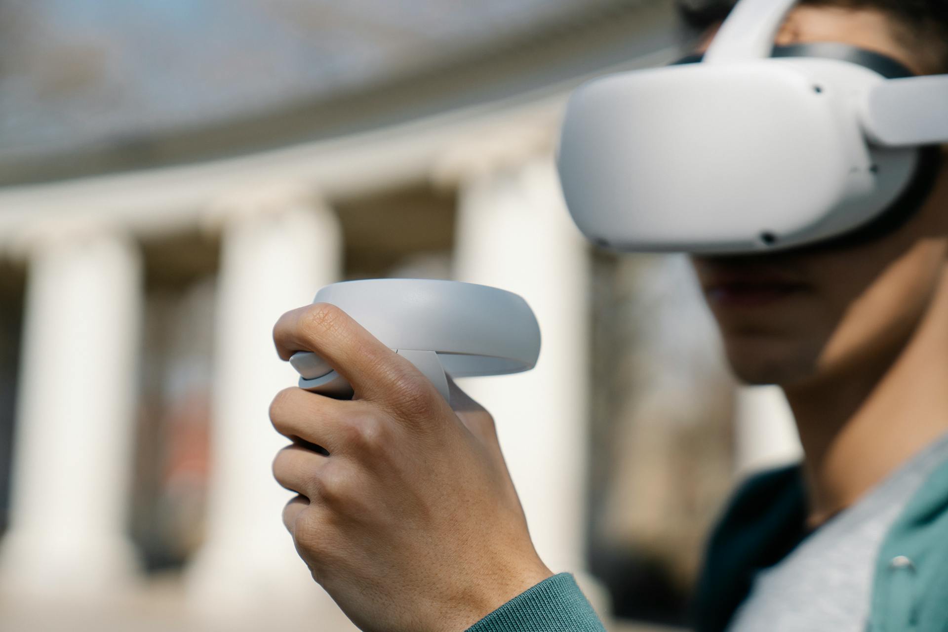 Crop young male in modern goggles of virtual reality using controllers while standing near building on street on daytime