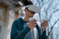 Low angle of young male in casual clothes experiencing virtual reality while standing on street near building holding controllers