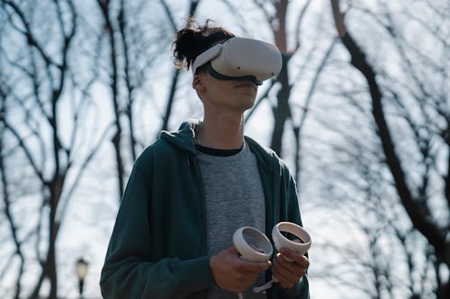 Anonymous male in virtual reality headset enjoying game on blurred background of leafless trees