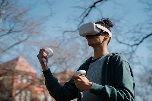 Man in virtual reality goggles with controllers playing video game in town on sunny day