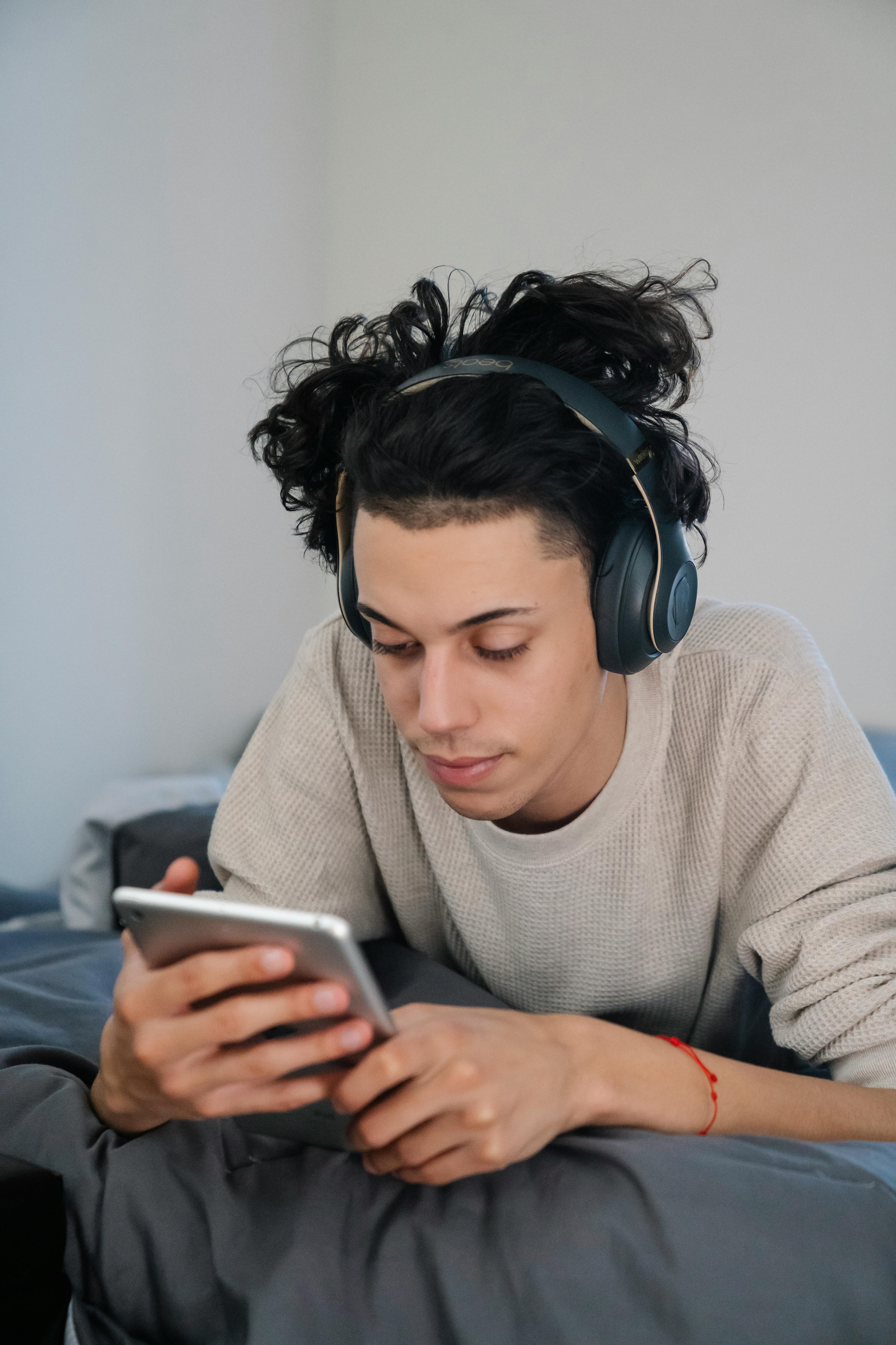 ethnic man in headphones surfing internet on smartphone on bed