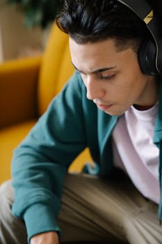 A young man with headphones sitting indoors, absorbed in music while relaxing at home.