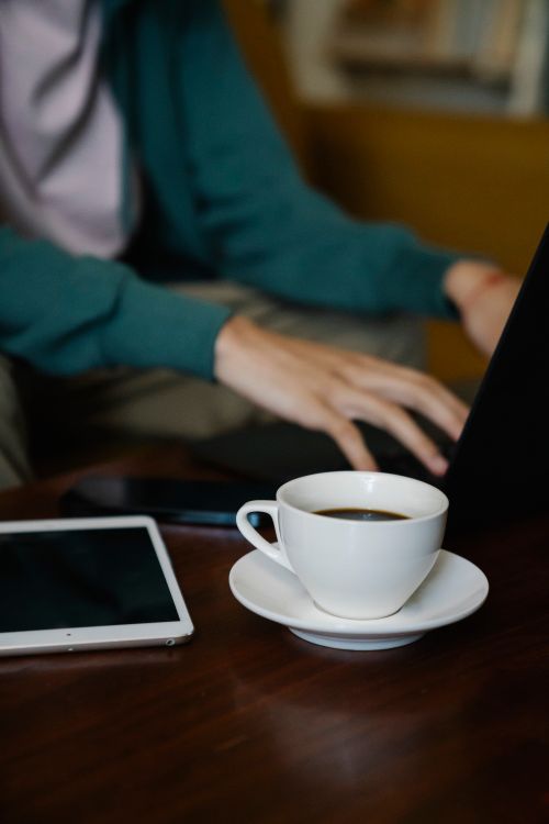Free Crop unrecognizable male remote employee working on netbook at table with cup of coffee and tablet in house room Stock Photo
