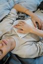 From above of crop ethnic male with tablet and closed eyes listening to music from headphones on bed at home