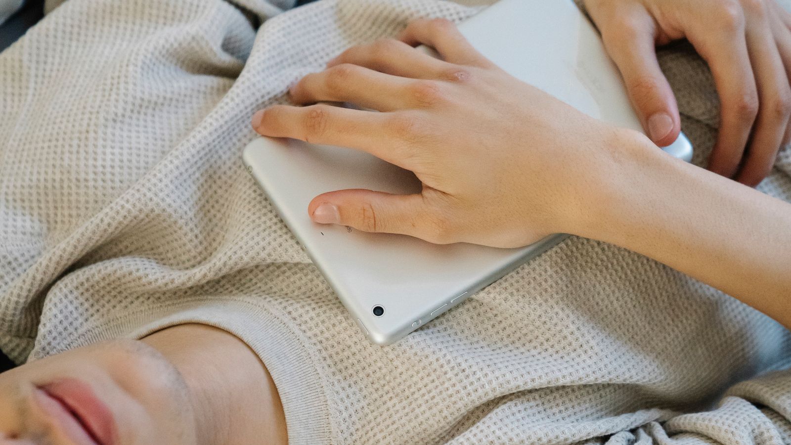 A young man lying on a bed with his eyes closed while wearing headphones beside a tablet