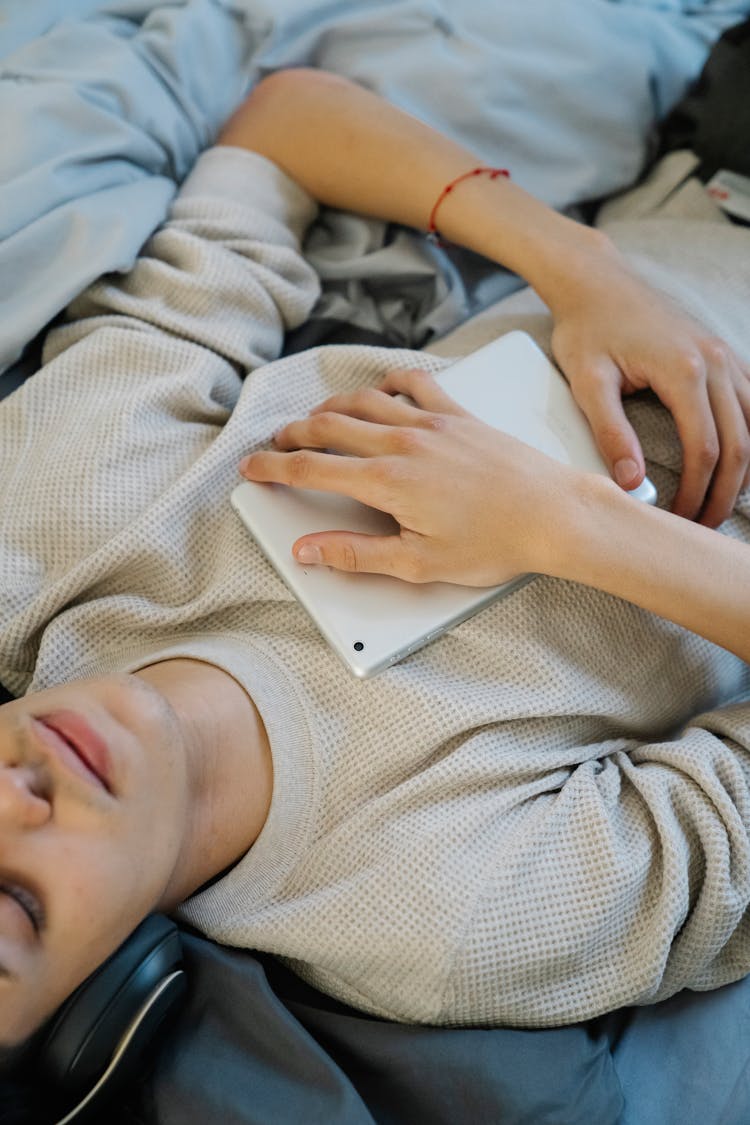 Crop Ethnic Man In Headset With Tablet On Bed