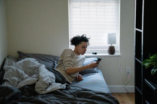 Free Ethnic man chatting on smartphone in bed at home Stock Photo