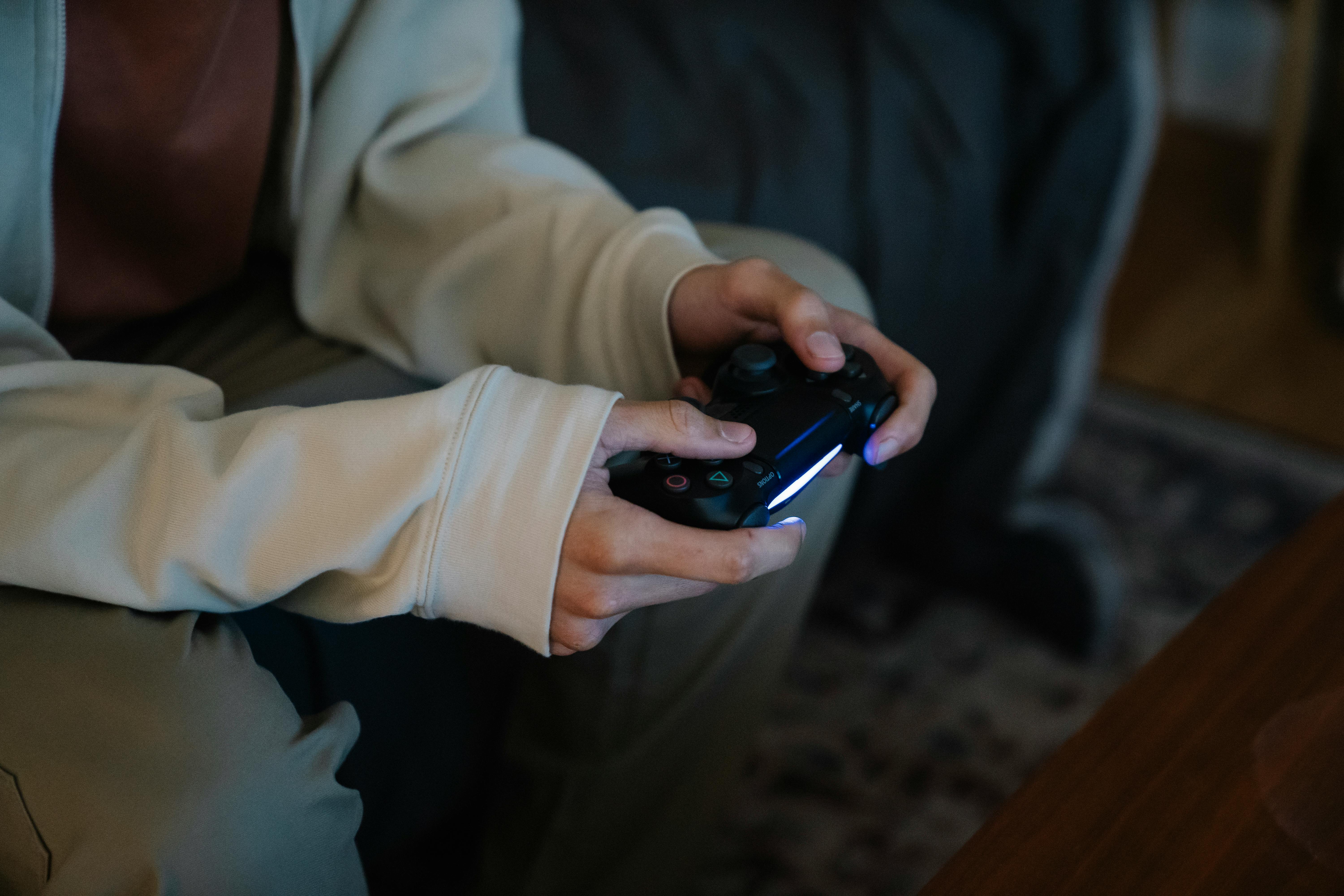 Crop unrecognizable man with joystick playing video game while sitting on couch in house room