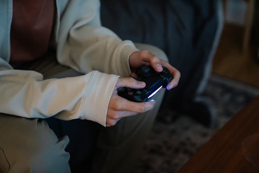 Crop unrecognizable man with joystick playing video game while sitting on couch in house room