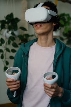 Male in virtual reality goggles with controllers playing video game while having free time in house
