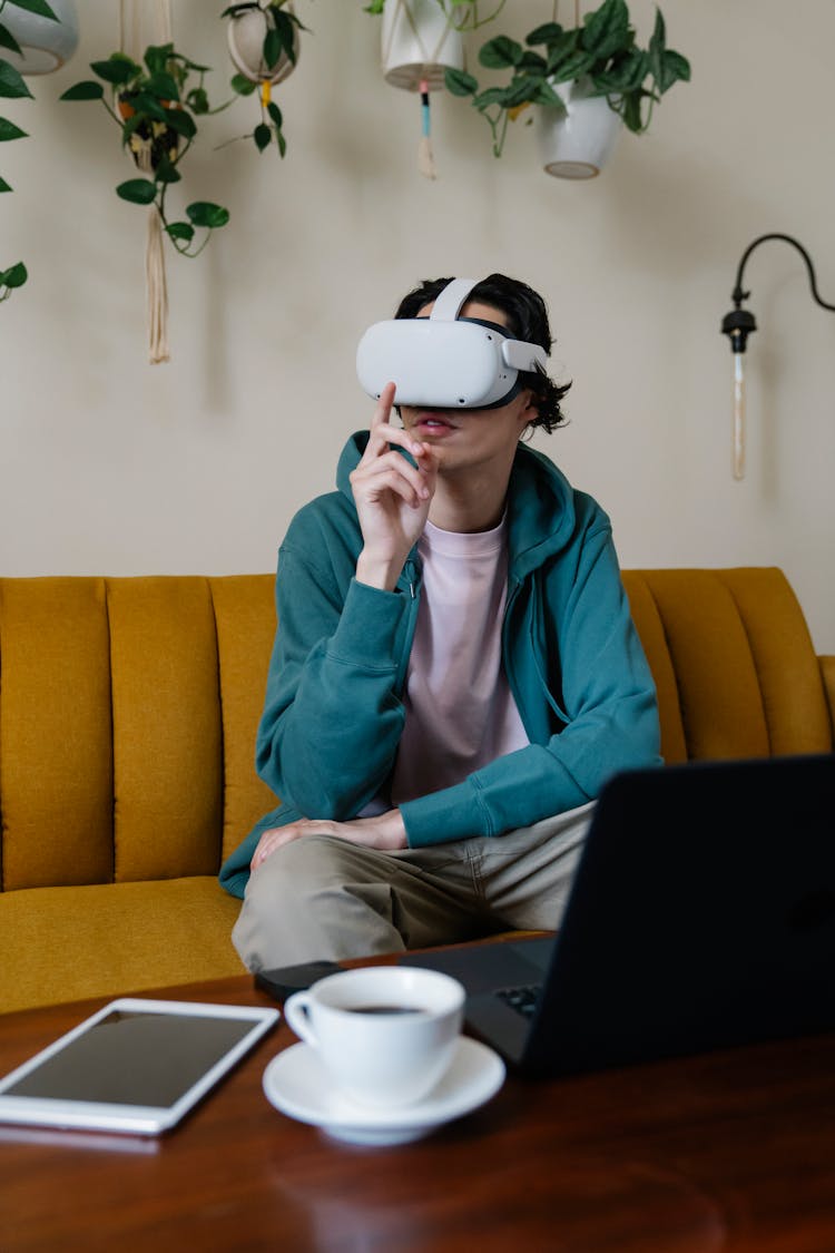 Man Experiencing Virtual Reality In Goggles Against Gadgets At Home