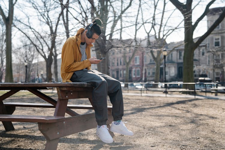 Trendy Ethnic Man In Headset Chatting On Smartphone In Park