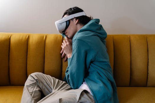 A young man in a hoodie rests with a VR headset on a yellow sofa, enjoying virtual reality.