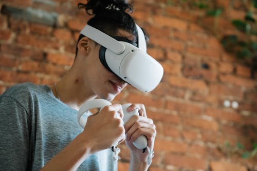 Gamer in VR headset playing video game against brick wall