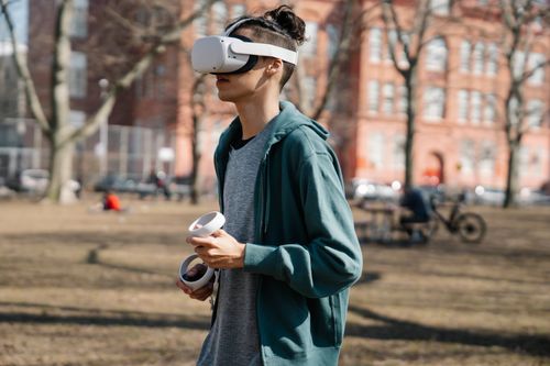 Free Person wearing VR headset in park, experiencing immersive virtual reality outdoors. Stock Photo