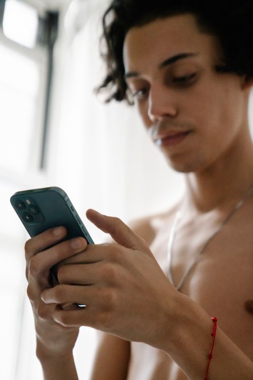 Free A topless young man focuses on his smartphone in a bright indoor setting. Stock Photo