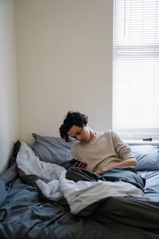 A young adult relaxing on a bed while using a smartphone in a cozy bedroom setting.