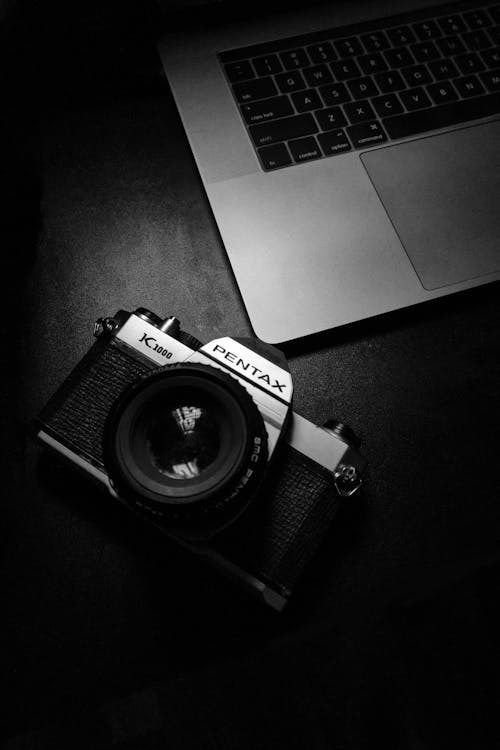 Free Close-Up Shot of a Digital Camera beside a Laptop on a Black Surface Stock Photo