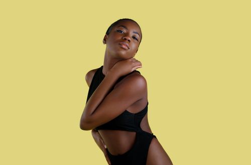 Free Graceful portrait of a woman in black swimwear posing against a vibrant yellow backdrop. Stock Photo