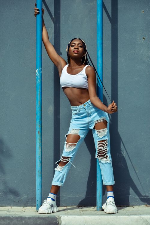 Free Fashionable woman in ripped jeans and crop top posing against a concrete wall. Stock Photo