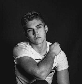Monochrome close-up of young male model in a pensive pose wearing a white shirt.