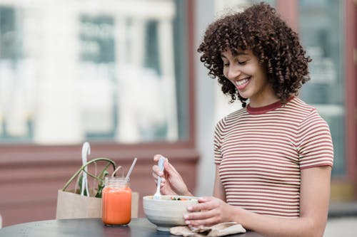 Happy ethnic woman at street cafe table with tasty lunch