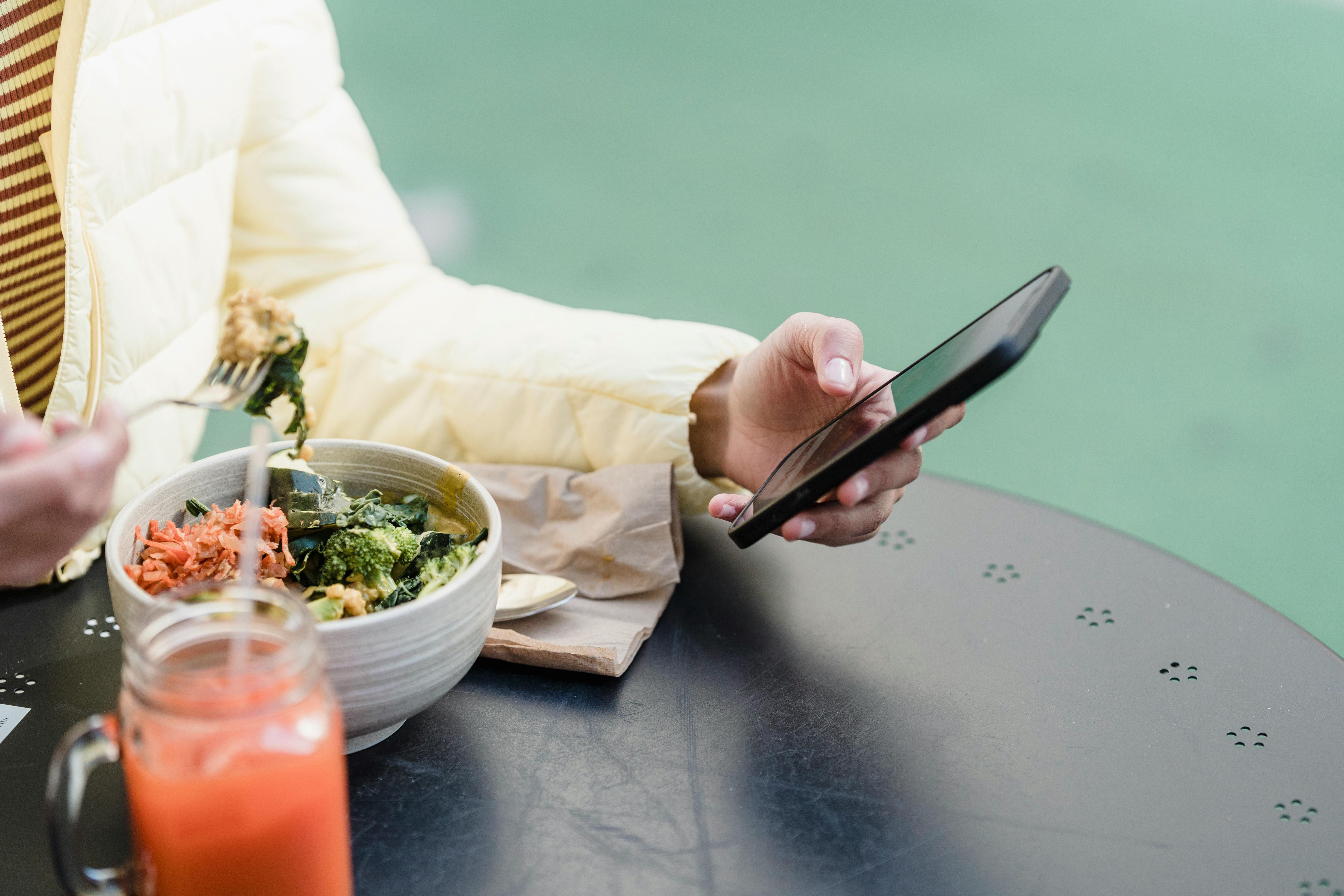 crop woman with smartphone and vegetable salad in street cafeteria