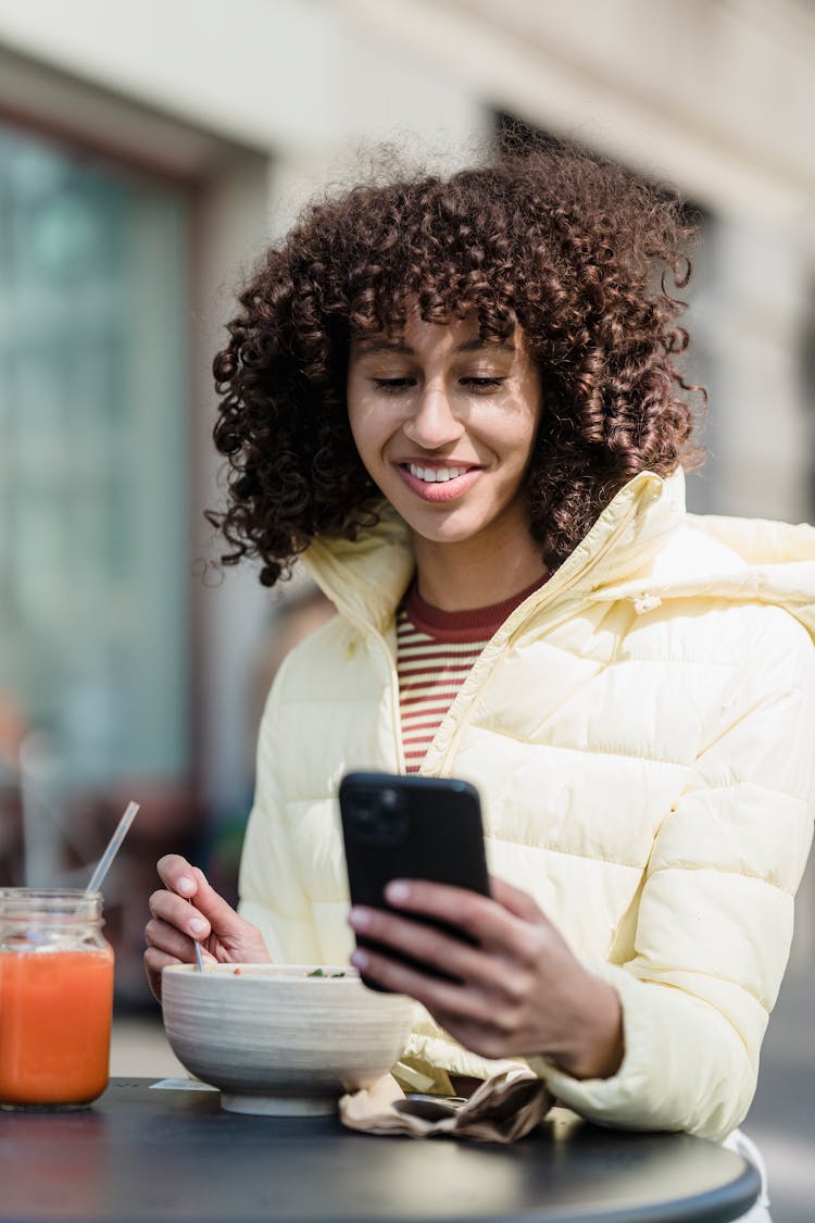 Cheerful Ethnic Woman With Smartphone Having Lunch In Street Cafe