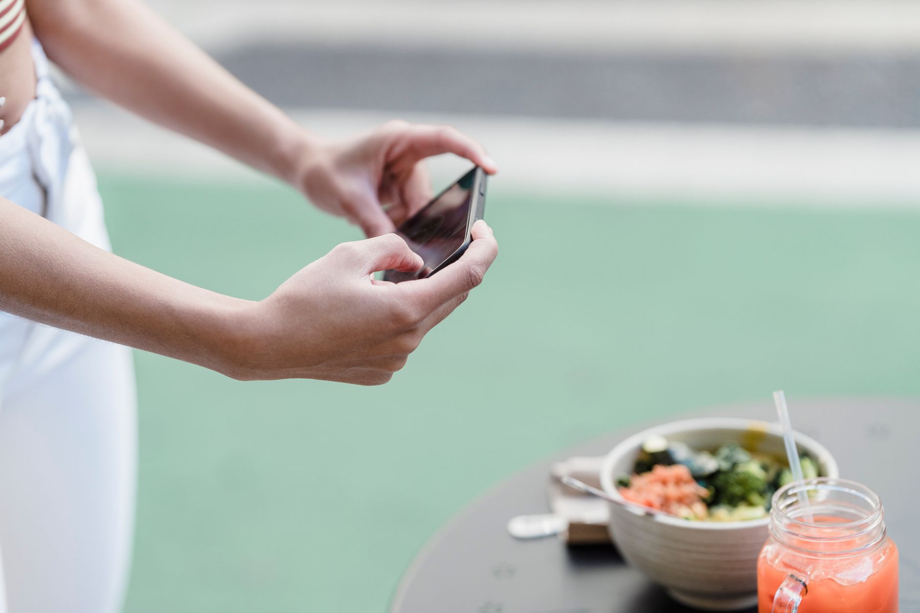 Crop unrecognizable female blogger taking photo of vegetable salad and smoothie on cellphone in street cafeteria