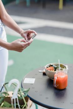 Crop anonymous female blogger taking photo of delicious vegan salad and smoothie on mobile phone in urban cafe