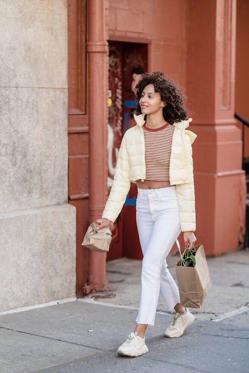 Free Content young ethnic female buyer with disposable bags strolling on walkway while looking away in town Stock Photo