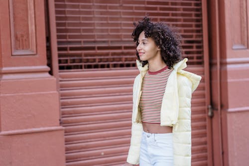 Smiling ethnic woman with curly hair against urban building