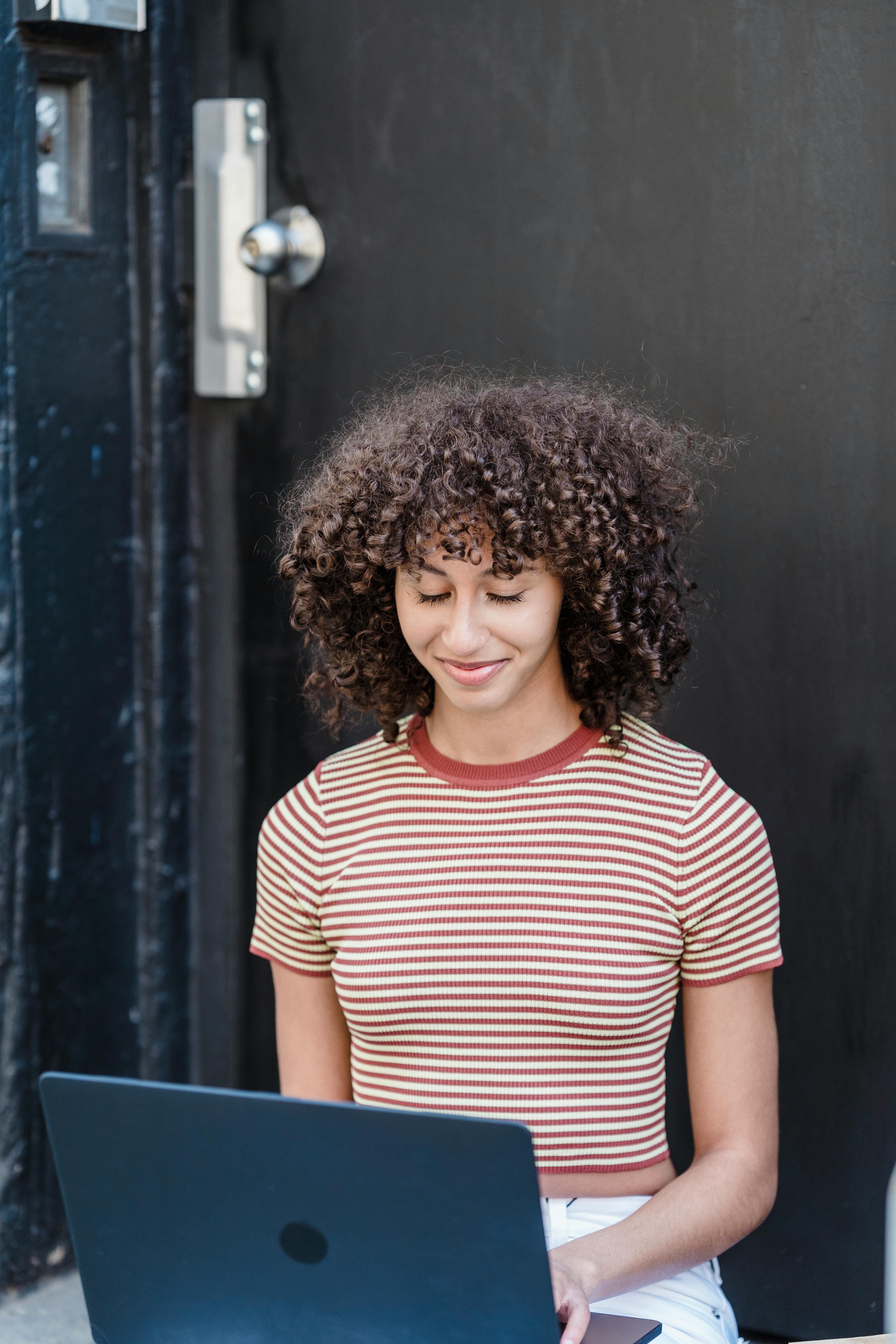 cheerful ethnic woman browsing laptop on street